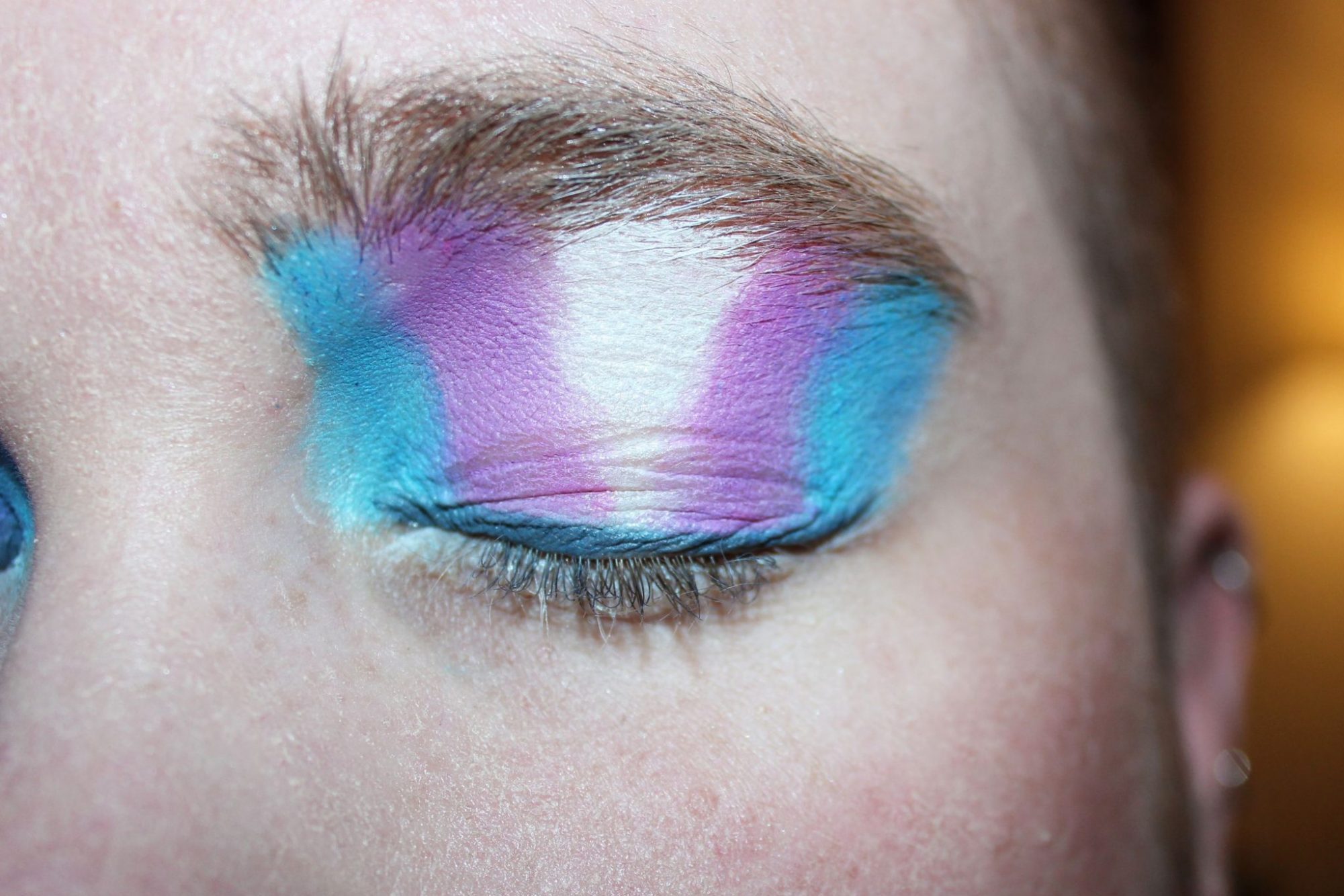 Photo of a trans person with eyeshadow that is the color of the transgender pride flag