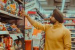 A man picking a food item off the shelf in a dollar store.