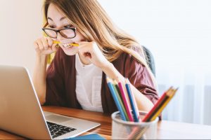 Young woman biting pencil in frustration while looking at laptop screen. Online writing classes can be tough.