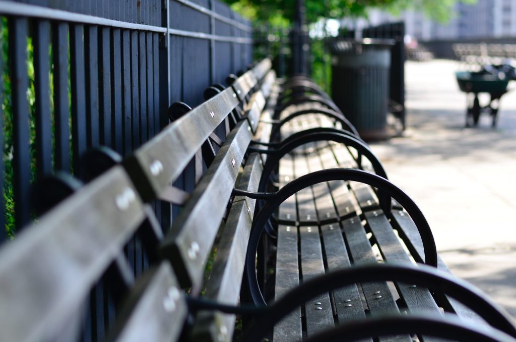 In article about homeless people and hostile architecture, a photo of a bench with extra armrests installed