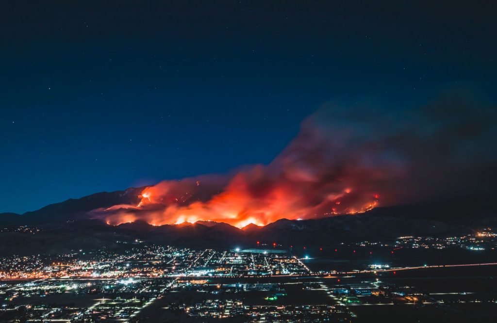 In an article about West Coast wildfires. The image is of a fire behind a California town.
