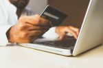 In an article about credit card debt, a person holding a credit card in front of a laptop
