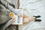 for an article about self-care, woman holding a cup of coffee and an open book on her lap