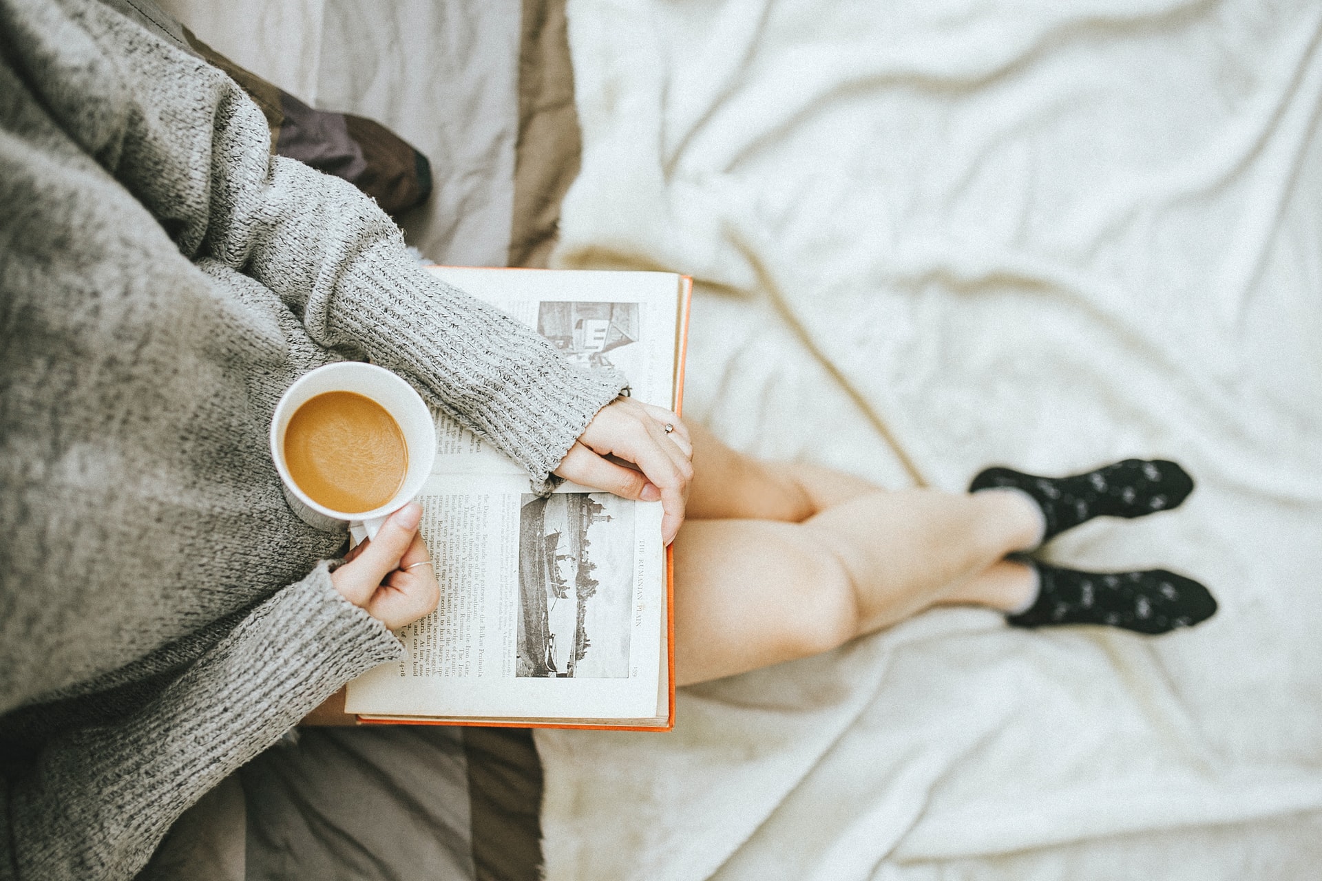 for an article about self-care, woman holding a cup of coffee and an open book on her lap