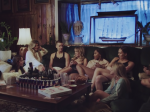 Olivia O'Brien and a group of friends sitting together in a living room setting for a music video from her album Episodes: Season 1. (Image via Google Images)