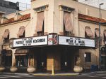 In an article about COVID-19 and its effect on television, a picture of a movie theater with a warning to wear a mask