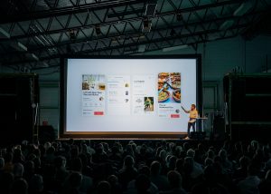 In an article about PowerPoint presentations, someone standing in front of a presentation screen