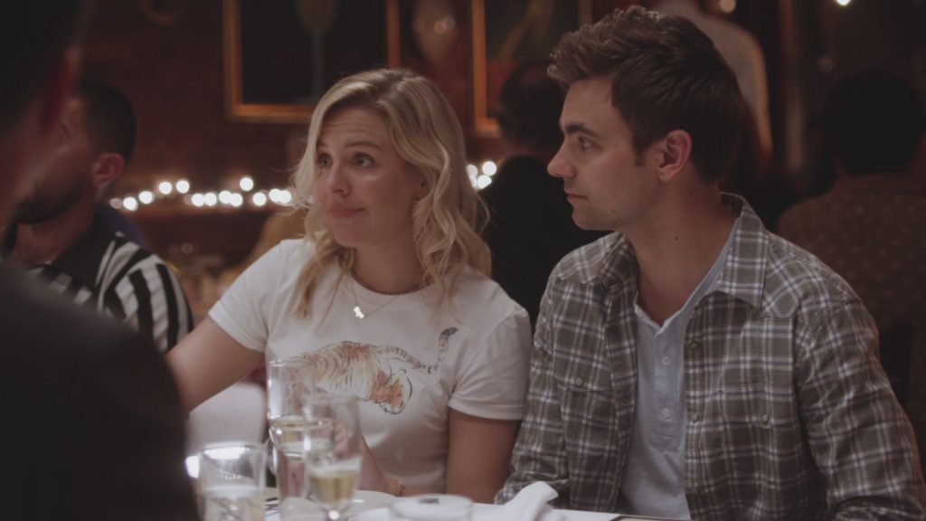 In an article about series the Other Two, a man and a woman sit at a restaurant table next to each other.