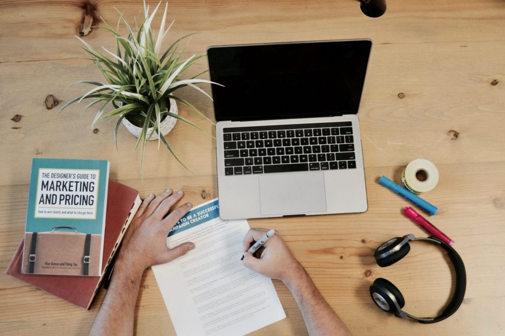 In an article about plagiarism, someone writing an essay on a desk with a laptop, headphones and book