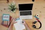 In an article about plagiarism, someone writing an essay on a desk with a laptop, headphones and book