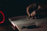 in article about college writing workshop, a hand writing into a notebook