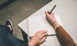 in article about essays, someone writing in an empty notebook