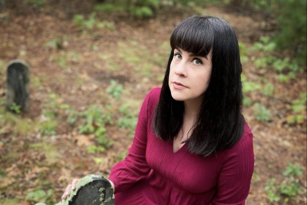 A photo of YouTuber and mortician Caitlin Doughty in front of an old headstone.