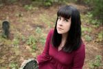 A photo of YouTuber and mortician Caitlin Doughty in front of an old headstone.