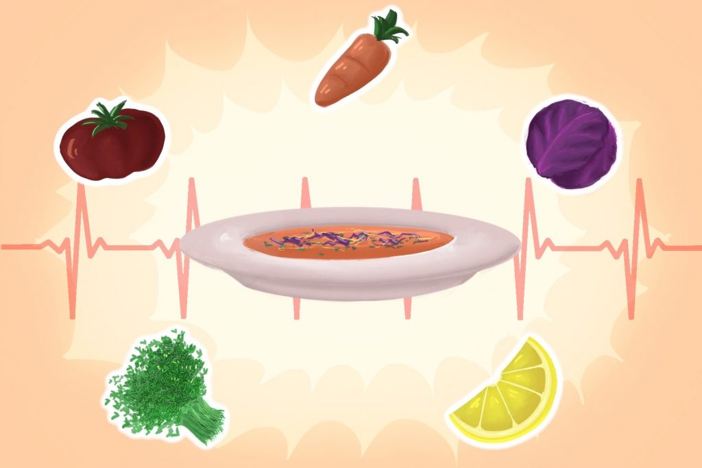 White saucer filled with vegetable soup that has various fruits and veggies encircling the plate