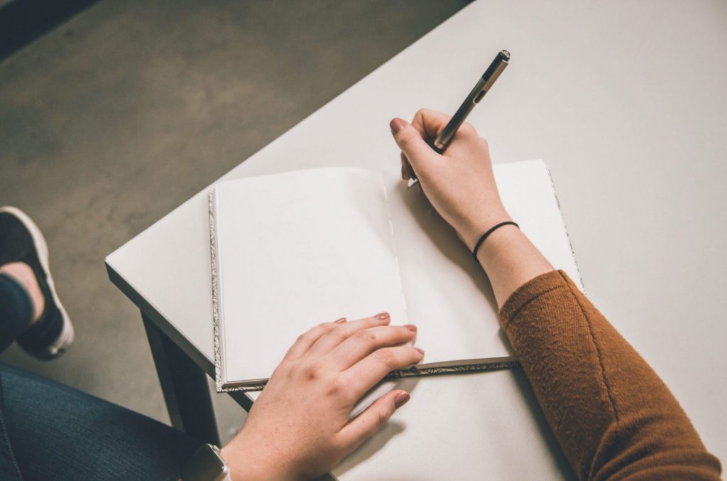 in an article about writing a thesis statement, a person writing in a notebook at their desk
