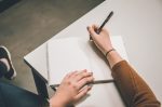 in an article about writing a thesis statement, a person writing in a notebook at their desk