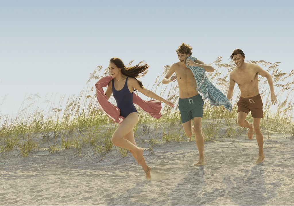 A screenshot from The Summer I Turned Pretty shows three young people running down a sand dune.