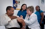 in article about healthcare, a person giving a shot to another person with two others in the background