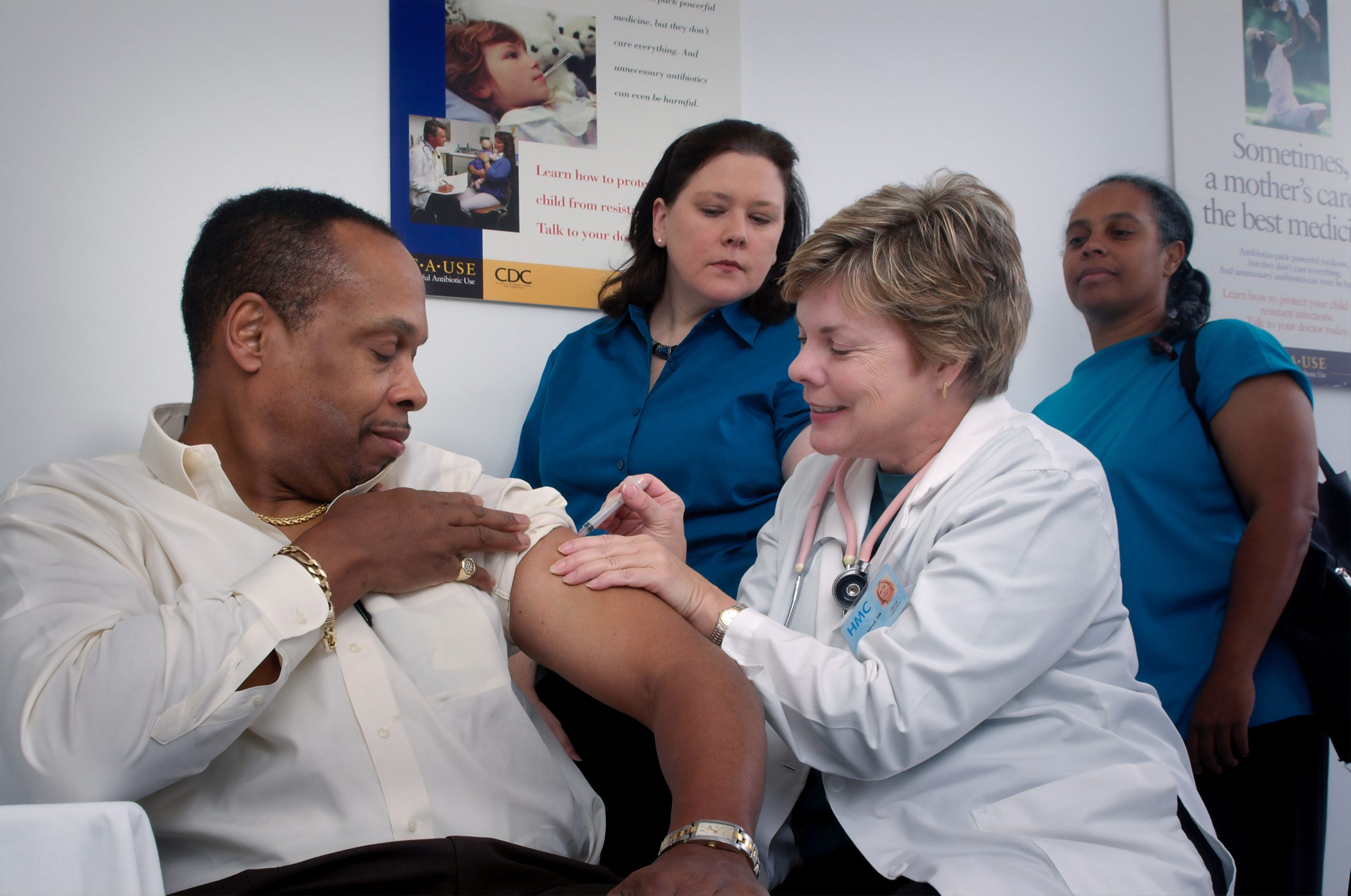 in article about healthcare, a person giving a shot to another person with two others in the background