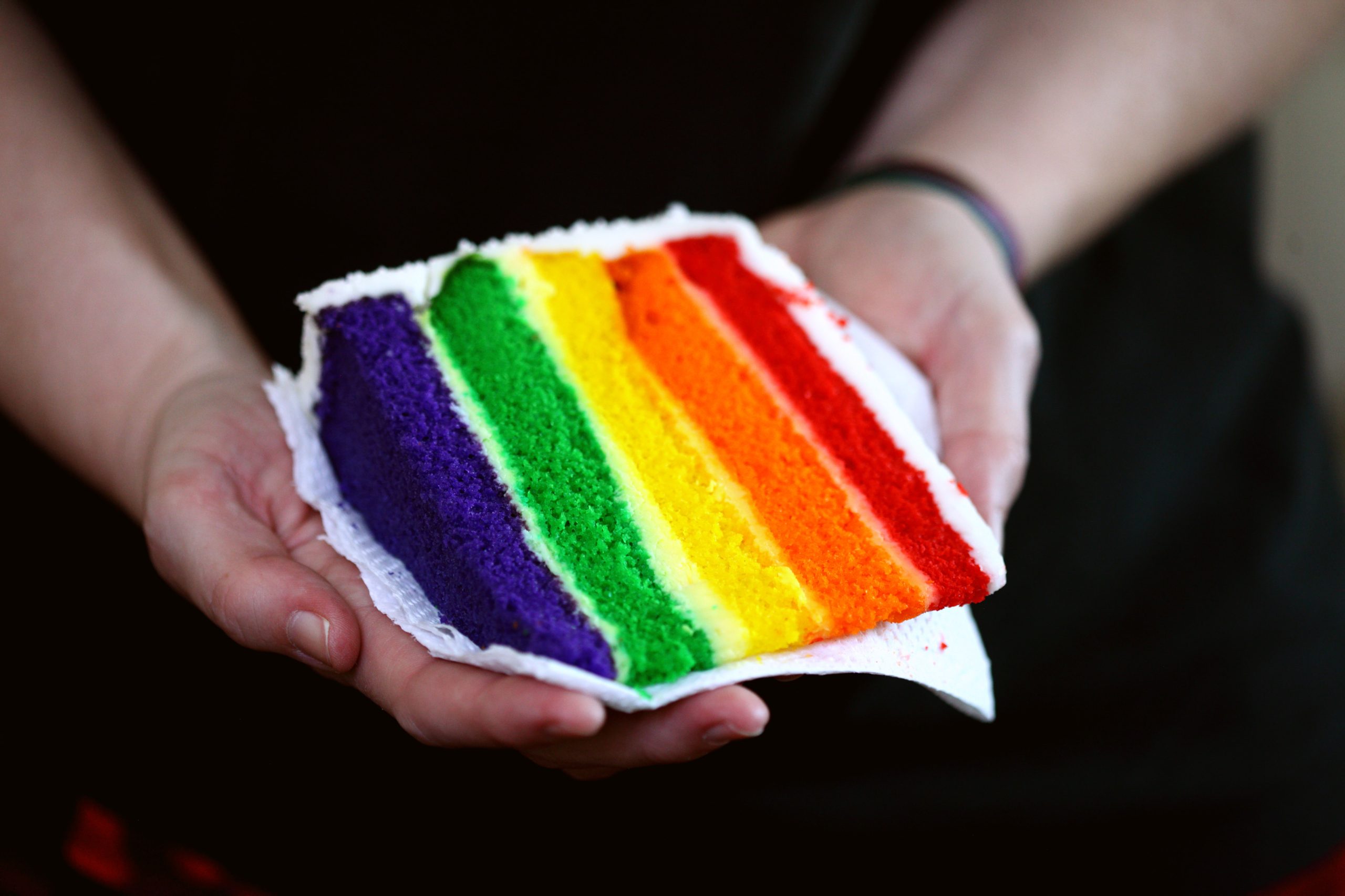 in article about national coming out day, a person holding a rainbow cake