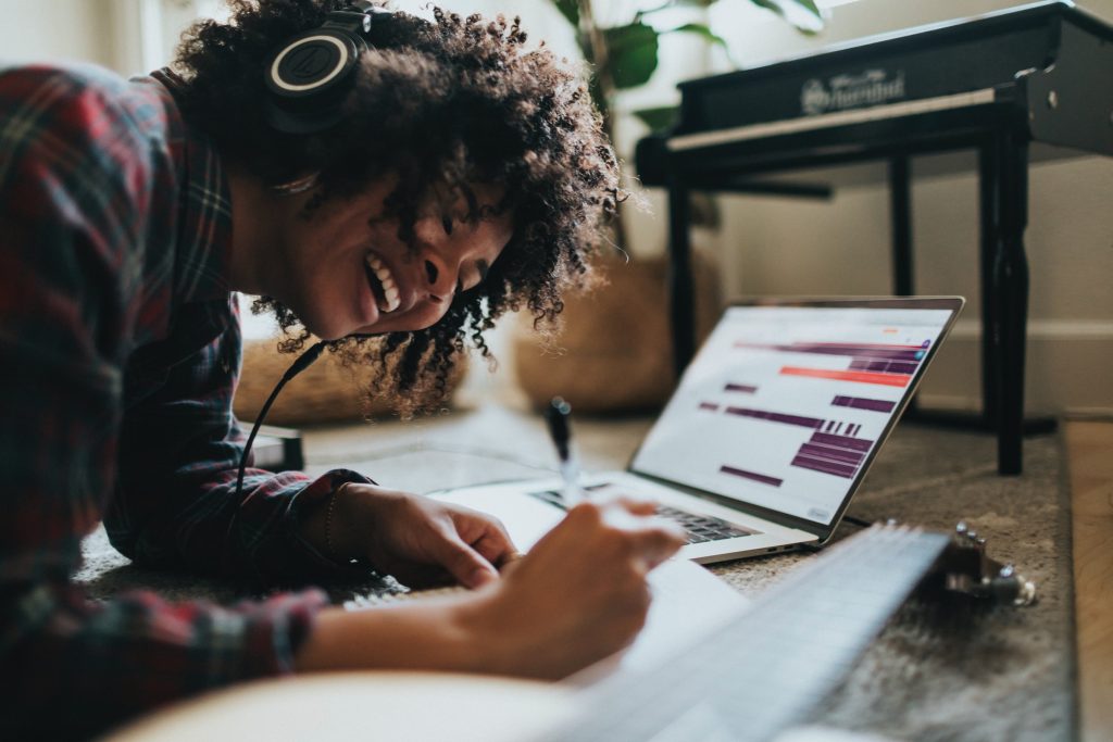 in article about bopdrop, woman laying on the ground writing in notebook while listening to music