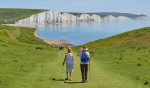 in an article about saving for retirement during inflation, an older couple hikes in front of a lake.