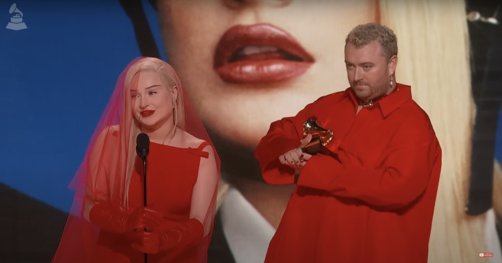 Kim Petras and Sam Smith in red outfits accepting their award for "Unholy" at the Grammy Awards.