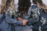 In an article on Women's History Month is a photograph of three women in jean jackets facing backward and holding white flowers.
