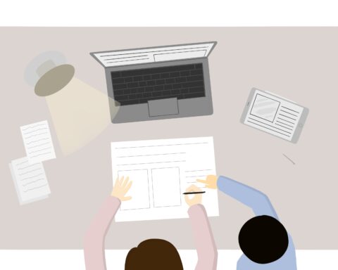 In an article about tutoring, one person types on a laptop while another person guides them with their hand on their shoulder.