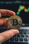 Hand holding bitcoin in front of computer chart