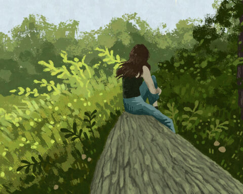 In an article about reconnecting with nature a girl with brown hair sits sits on a log among trees and other greenery.