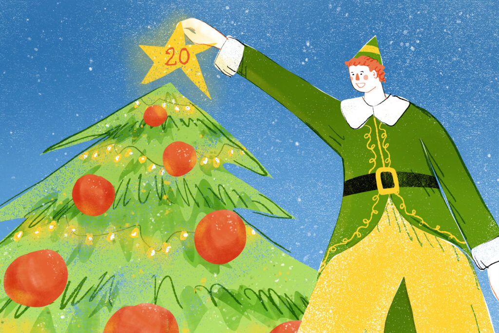 In an article about "Elf" 20 year anniversary, a man with orange hair and green coat and yellow stockings places a glowing yellow star with the number "20" on it" atop a green Christmas tree with red ornaments and bright yellow lights.