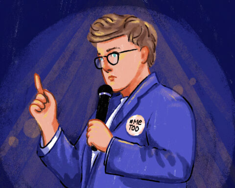 Against a dark purple background, a woman with short hair and glasses speaks into a microphone with her finger pointed up, with a #MeToo button pinned to her purple blazer.