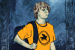 For an article about the Percy Jackson TV series, a boy with mid-length brown hair wears a bright orange-yellow shirt with a pegasus (winged horse) on it while carrying a dark backpack. He stands against a blue, water-like, crinkly paper background with a Greek-style border along the left and right side.