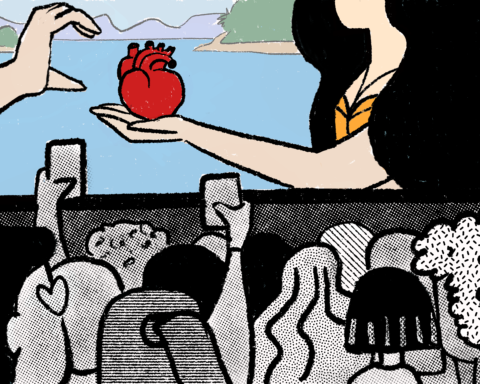 Woman giving an anatomical heart to someone while a crowd watches and records on their phones.